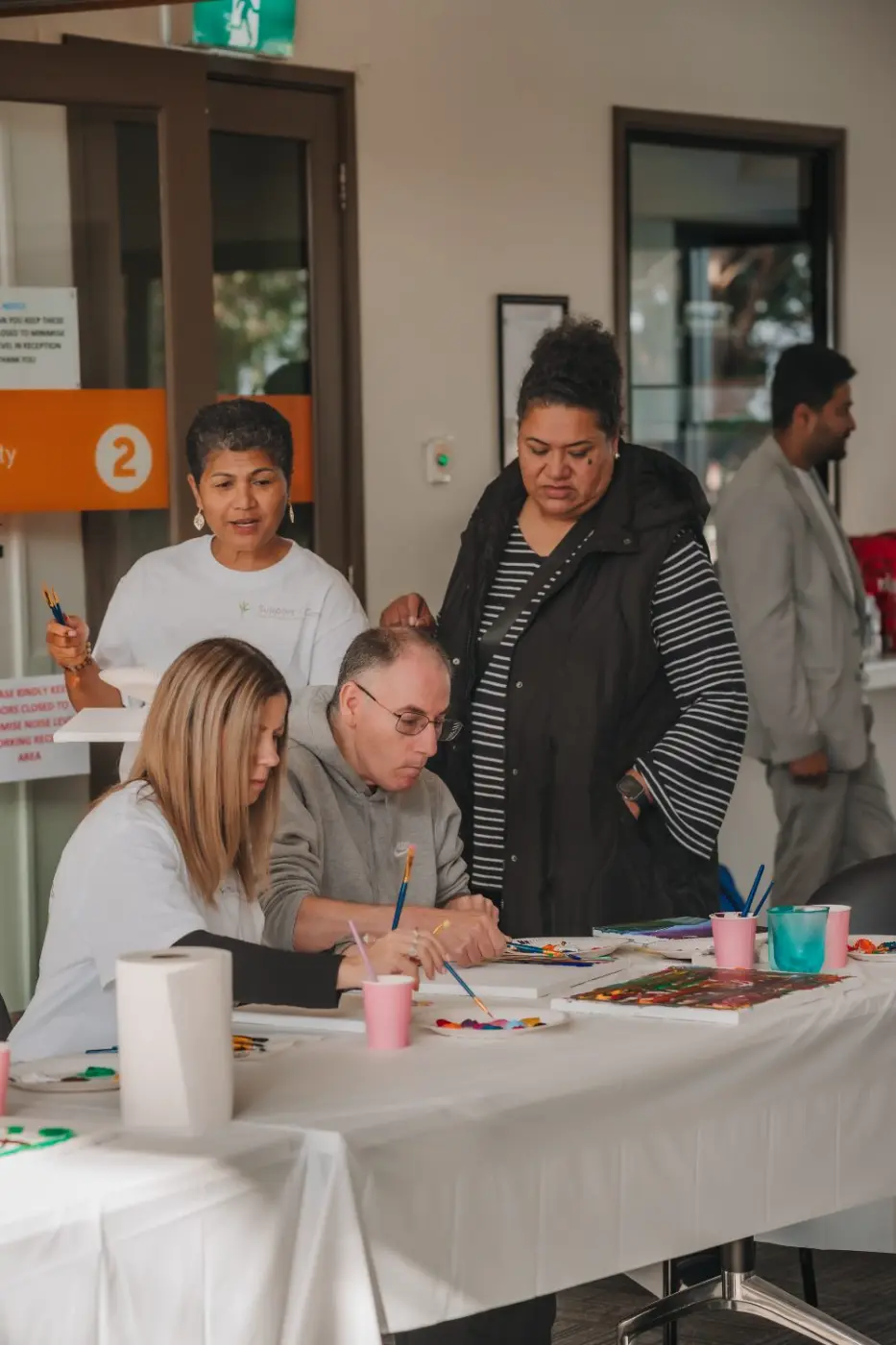 Participants and support workers painting together at a long table