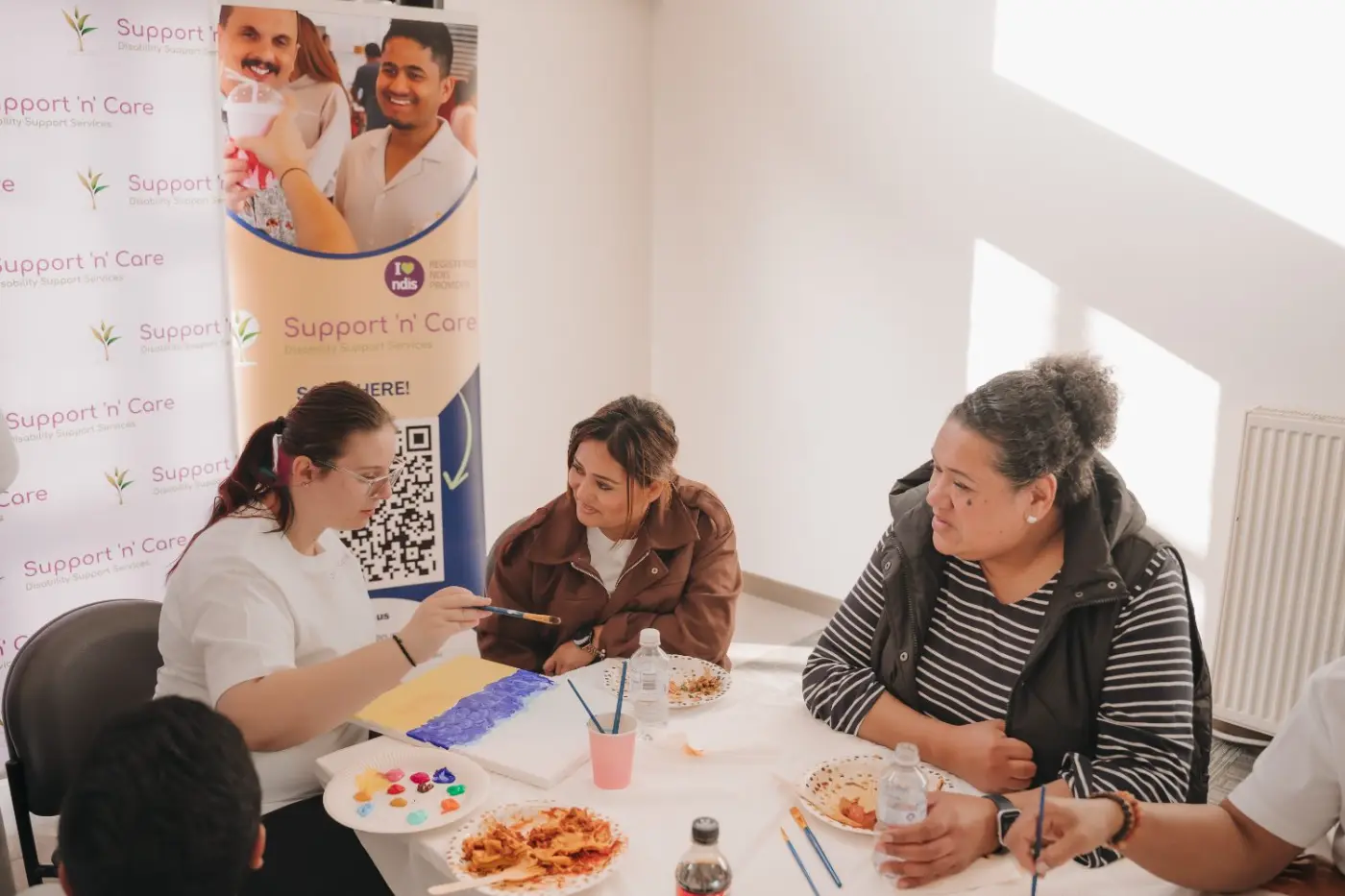 Participants and support workers painting together around a table