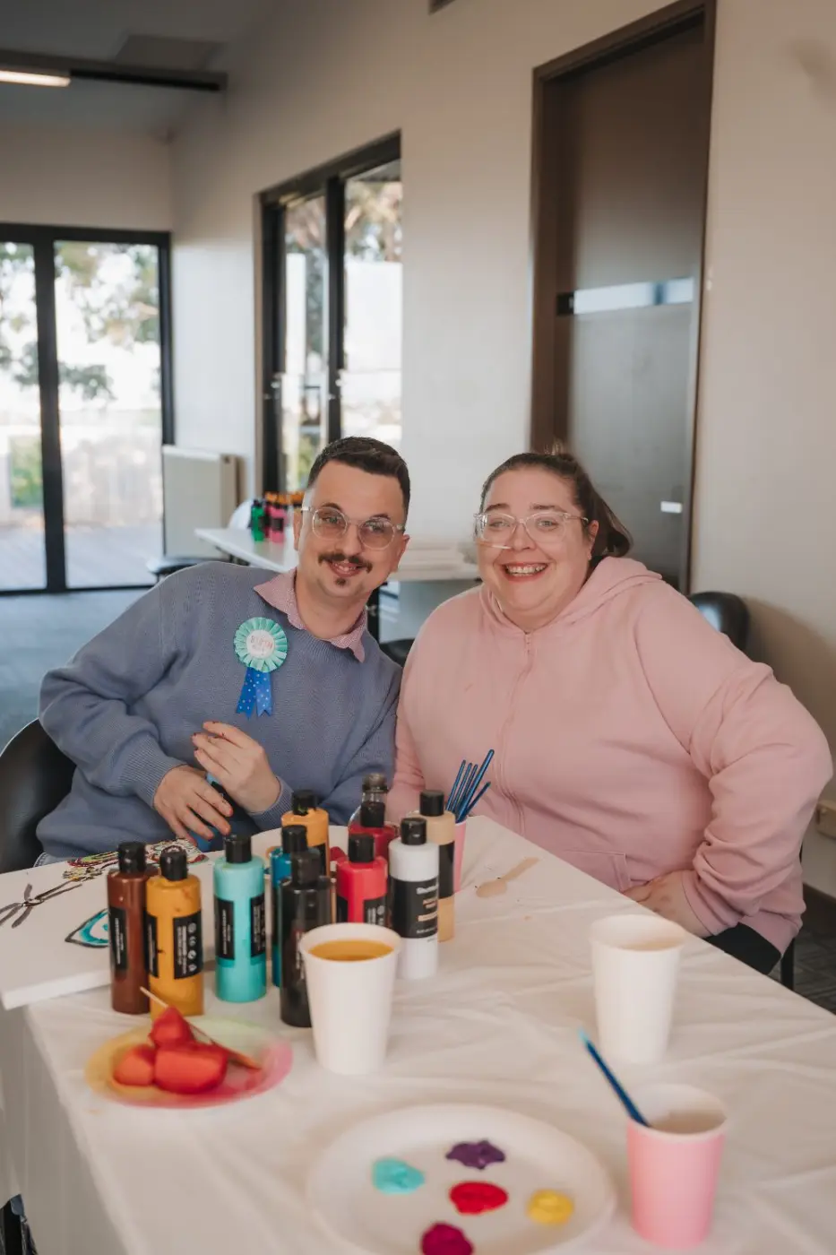 Participant and support worker smiling together at an art table