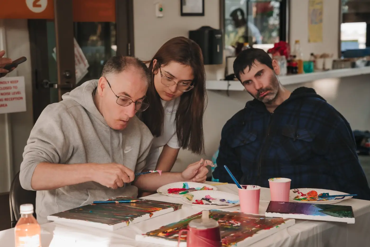 Participants and a support worker painting together at a group art activity