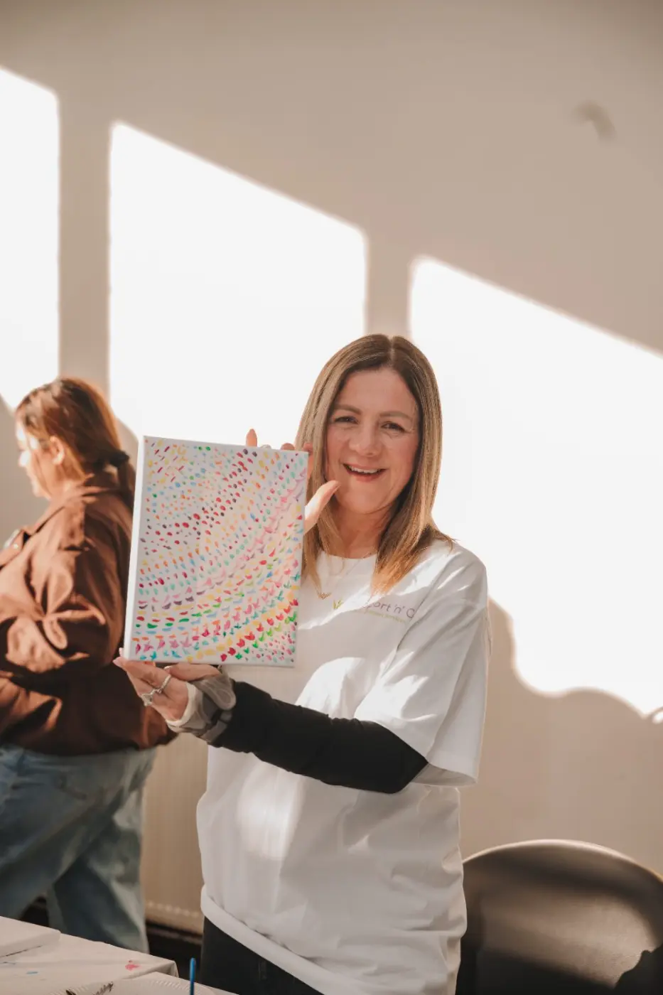 Support worker holding up a colourful painting